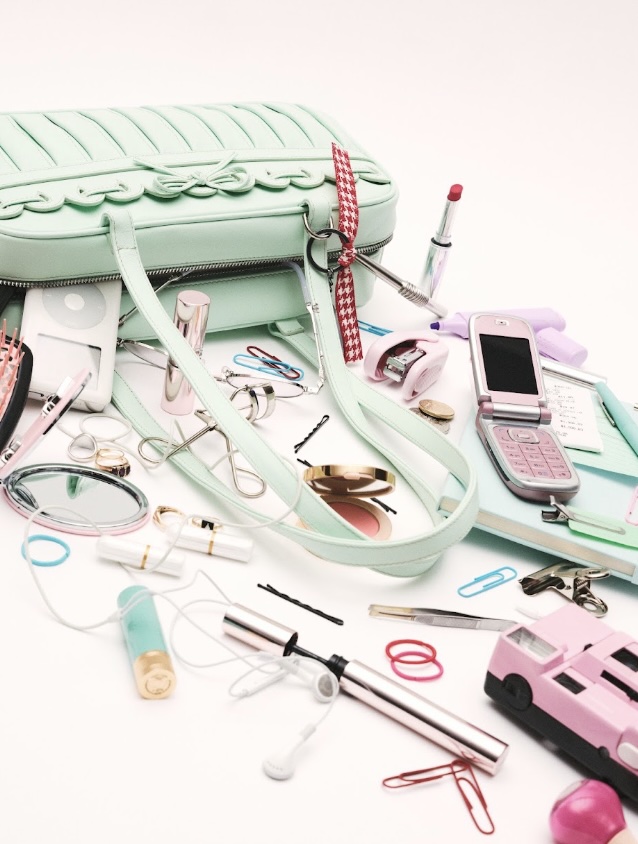 A mint green quilted handbag with pastel beauty accessories and everyday items spilled out onto a white surface.